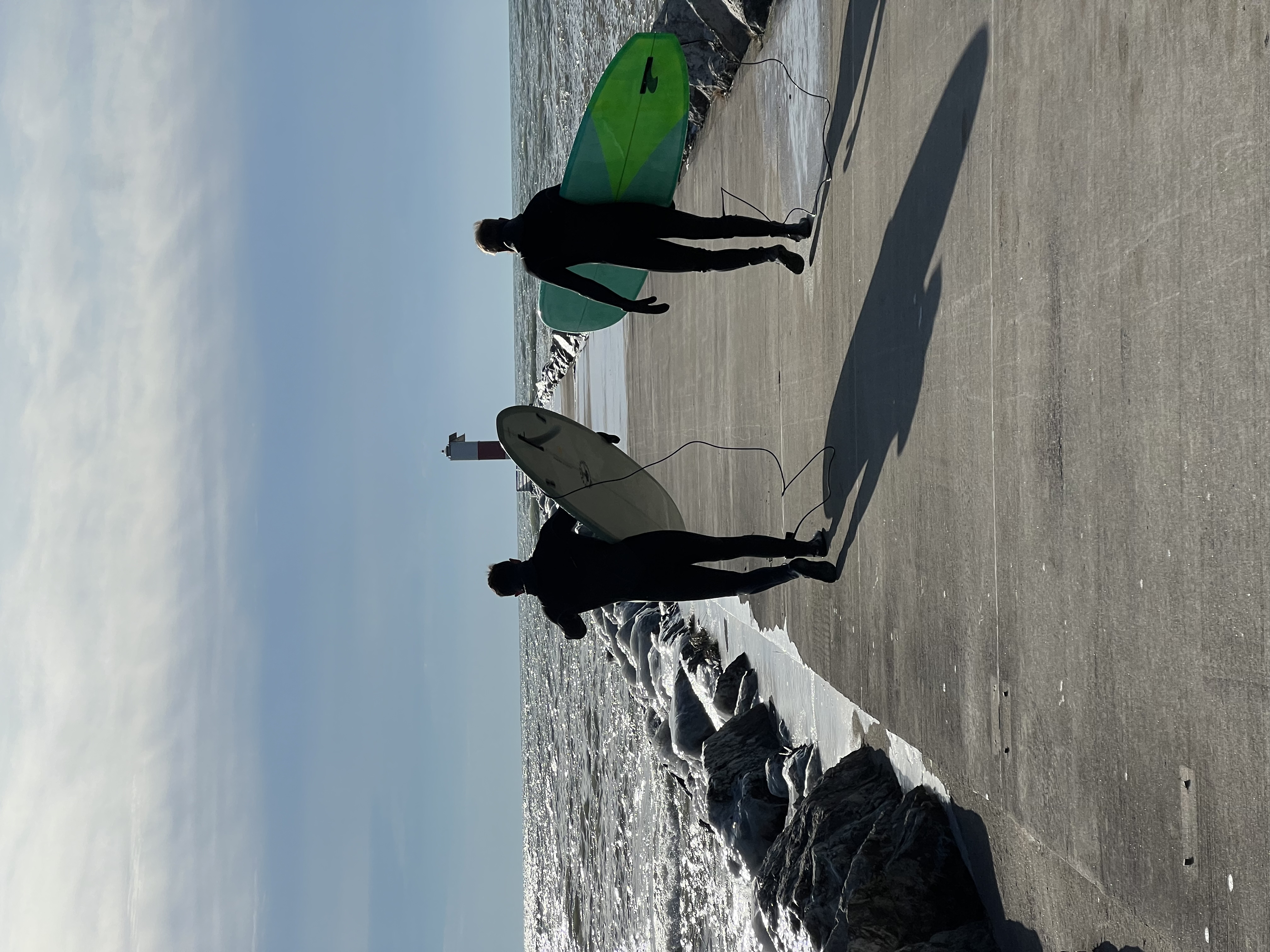 Two surfers carrying boards along a Lake Michigan pier